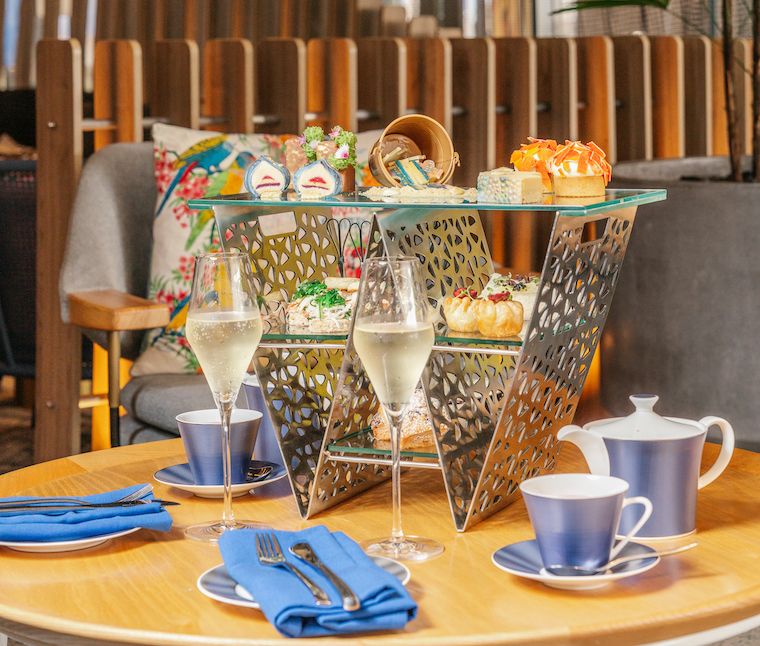 A high tea stand with sweets and savouries, two glasses of bubbles and teacups